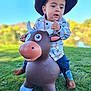 Riley is registered to the contest to win money with this photo: toddler, child, cowboy_hat, boots, plush_toy, outdoor, grass, blue_sky, toy_bull, play, cute, portrait, young_child, daylight, nature, fun, costume, jeans, holding, smiling