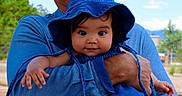 Presley is registered to the contest to win money with this photo: baby, child, blue_hat, blue_clothing, adult, outdoor, nature, trees, sky, portrait, cute, smiling, arm, hand, person, holding, face, expression, sunlight, daytime