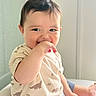 baby, child, dinosaur_clothing, cute, smiling, hand_in_mouth, sitting, indoors, shorts, tshirt, window, light, skin, portrait, happy, young_child, infant, casual, comfort, playful