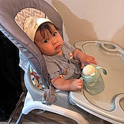 Lukas joined the competition — help win amazing prizes! baby, high_chair, sippy_cup, hat, striped_clothing, indoor, floor, wall, table, child, person, furniture, curious, feeding, seat, young_child, expression, holding, drink, casual