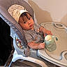 Lukas joined the competition — help win amazing prizes! baby, high_chair, sippy_cup, hat, striped_clothing, indoor, floor, wall, table, child, person, furniture, curious, feeding, seat, young_child, expression, holding, drink, casual