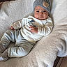 Lukas is registered to the contest to win money with this photo: baby, infant, blanket, hat, knitted_hat, clothing, striped_pants, white_shirt, floor, wooden_floor, cute, portrait, indoor, child, person, soft_texture, cozy, lying_down, comfortable, adorable