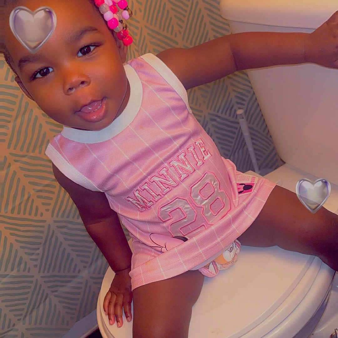Novah is registered to the contest to win money with this photo: child, toddler, girl, portrait, sitting, smiling, pink_jersey, basketball_jersey, beaded_hair, braids, hair_bow, heart_filter, bathroom, chair, indoors, patterned_wall, white_fixtures, casual_clothing, photograph, happy