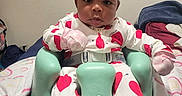 Novah joined the competition — help win amazing prizes! baby, infant, child, portrait, sitting, baby_seat, headband, bow, pajamas, hearts, pink, green, blanket, bedroom, indoor, furniture, face, dark_skin, looking_at_camera, cozy