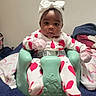 baby, infant, child, portrait, sitting, baby_seat, headband, bow, pajamas, hearts, pink, green, blanket, bedroom, indoor, furniture, face, dark_skin, looking_at_camera, cozy