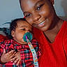 Novah joined the competition — help win amazing prizes! baby, child, mother, parent, infant, smiling, cuddling, portrait, indoor, red_clothing, plaid, pacifier, pacifier_clip, curly_hair, dark_skin, family, bedroom, selfie, pink_hearts, text_overlay
