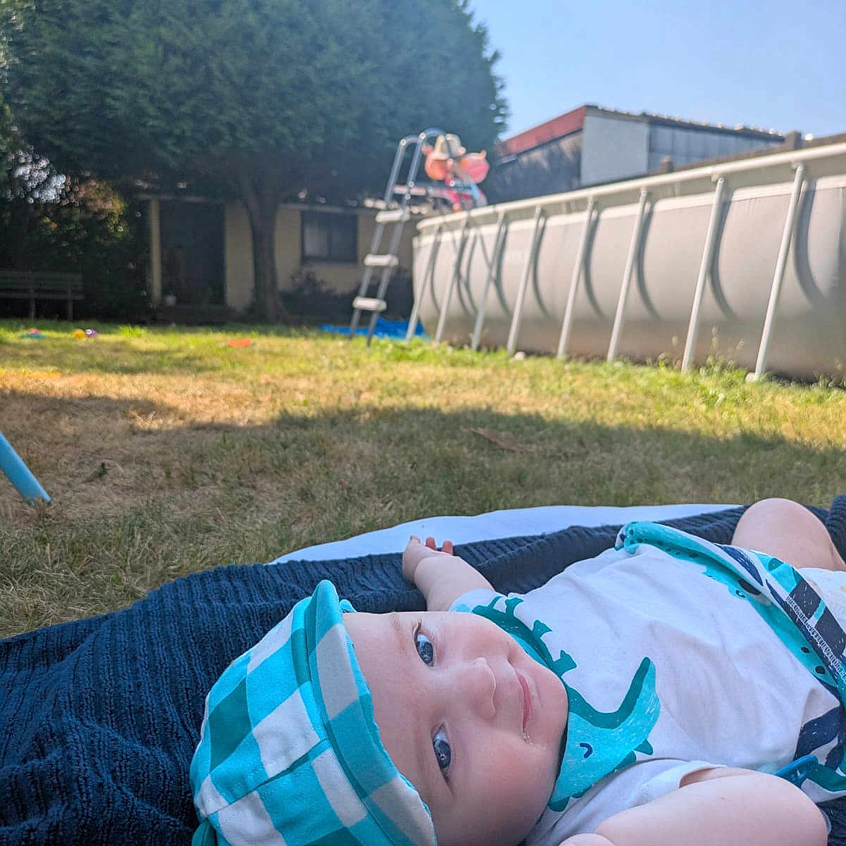 éveun a rejoint le concours — aidez-le/la à gagner de superbes lots ! baby, backyard, blanket, blue, child, clothing, daylight, grass, hat, infant, nature, outdoor, person, pool, recreation, relaxation, smiling, sunny, tree, white