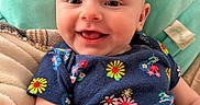 Athea is registered to the contest to win money with this photo: baby, smiling, infant, child, floral_clothing, blanket, cushion, happy, cute, face, portrait, indoors, comfort, soft, head, skin, person, apparel, seated, expression