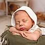 baby, sleeping, infant, white_bonnet, blanket, olive_green, fringe, resting, hands, face, closed_eyes, soft_light, portrait, indoor, cozy, peaceful, newborn, cute, skin, closeup