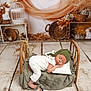 baby, sleeping, bed, blanket, pillow, wooden_floor, woven_basket, dried_flowers, green_cap, white_outfit, nursery, rustic, decor, soft_lighting, peaceful, infant, portrait, cozy, fabric, wood