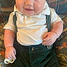 baby, child, smiling, blue_eyes, white_shirt, suspenders, dark_pants, pacifier, couch, patterned_fabric, sitting, cute, portrait, indoor, infant, happy, closeup, plump, hand, face