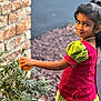 child, girl, flower, marigold, plant, pot, brick_wall, green_dress, pink_top, traditional_clothing, outdoor, smile, portrait, nature, young, leaf, pearl_necklace, hair, garden, daylight