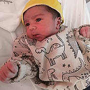 Dhash a rejoint le concours — aidez-le/la à gagner de superbes lots ! baby, infant, child, hat, yellow_hat, dinosaur_print, sweater, clothing, blanket, bed, fist, face, portrait, indoor, cute, newborn, lying_down, person, young_child, looking_away