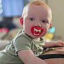 baby, child, pacifier, fangs, red_hair, blue_eyes, crawling, person, indoor, closeup, face, cute, infant, green_shirt, skin, expression, funny, mouth, tongue, background_blur