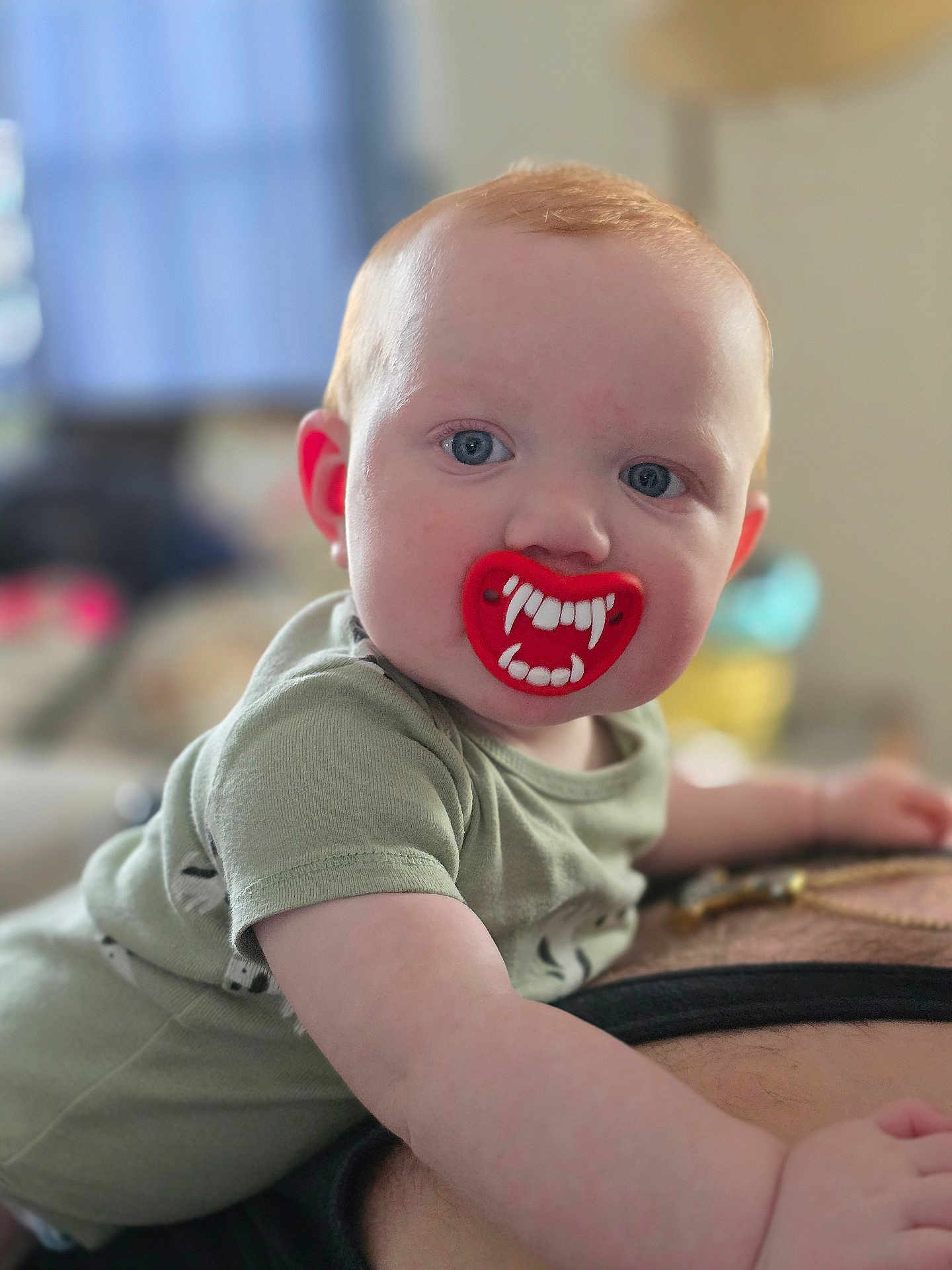Walker is registered to the contest to win money with this photo: baby, child, pacifier, fangs, red_hair, blue_eyes, crawling, person, indoor, closeup, face, cute, infant, green_shirt, skin, expression, funny, mouth, tongue, background_blur