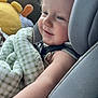 baby, child, car_seat, blanket, plush_toy, smiling, curly_hair, seatbelt, indoors, window, comfort, cute, infant, soft_toys, portrait, car_interior, child_safety, happy, closeup, relaxed