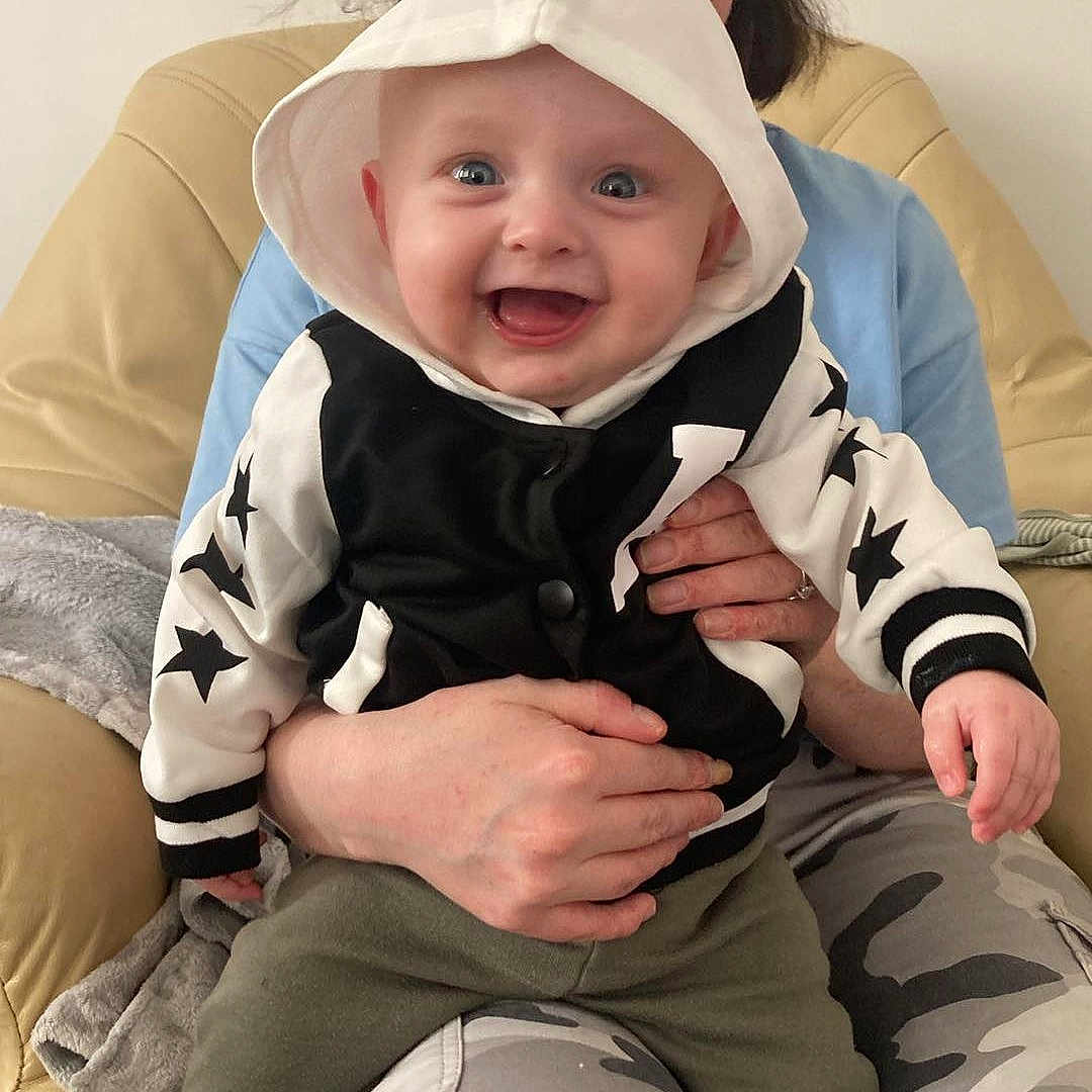 Grayson joined the competition — help win amazing prizes! baby, babylaughing, clothing, coat, face, happy, hat, head, hood, hoodie, knitwear, pants, person, photography, portrait, sitting, sweater, sweatshirt