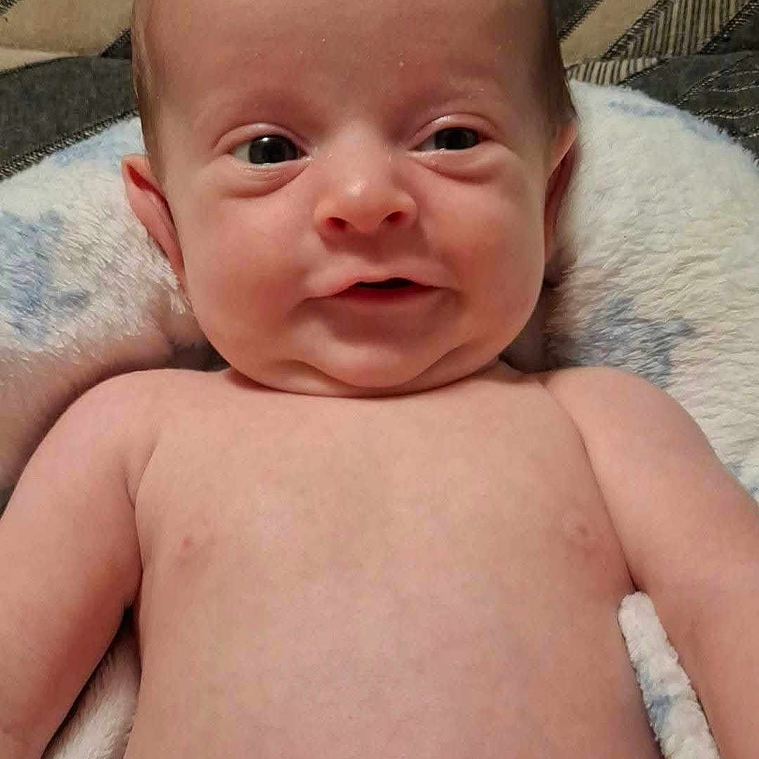Bennett is registered to the contest to win money with this photo: baby, newborn, child, infant, portrait, smiling, happy, lying_down, blanket, cushion, diaper, indoor, home, face, eyes, head, skin, bedding, patterned_background, photography