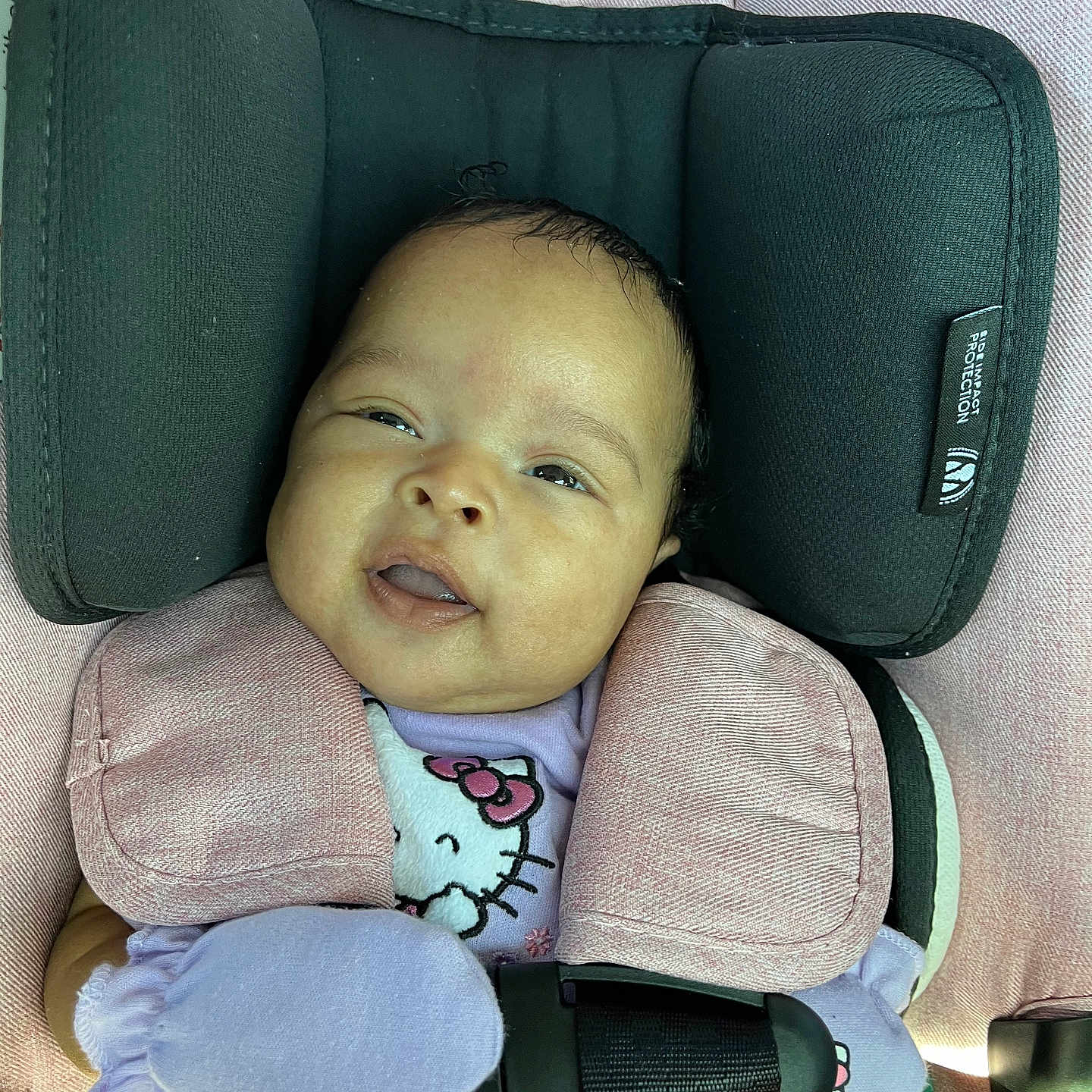 Jaliah joined the competition — help win amazing prizes! baby, infant, child, car_seat, safety_harness, portrait, face, eyes, smiling, seated, pink_clothing, hello_kitty, bib, mittens, cushion, vehicle_interior, travel, indoors, close_up, safe