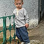 Adil a rejoint le concours — aidez-le/la à gagner de superbes lots ! child, toddler, boy, striped_shirt, baggy_jeans, sneakers, iron_fence, concrete_wall, outdoor, standing, serious_expression, short_blond_hair, portrait, candid, sidewalk, grass, urban_setting, texture_wall, hand_on_fence, full_body