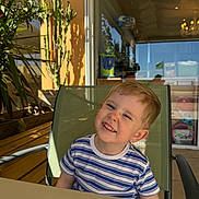 Adil a rejoint le concours — aidez-le/la à gagner de superbes lots ! child, boy, smiling, striped_shirt, green_chair, table, sunlight, shadow, cactus, plant, orange_wall, outdoor, daylight, scraped_nose, happy, casual, portrait, seated, blond_hair, playful