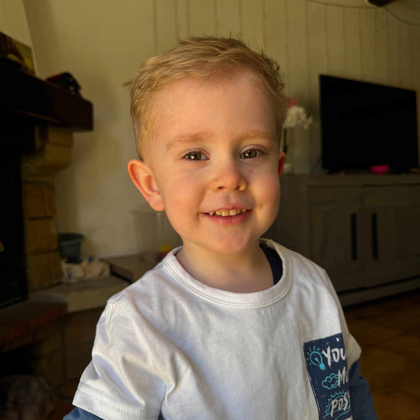 Adil is registered to the contest to win money with this photo: blond_hair, boy, candid, child, cute, eyes, face, fireplace, floor, furniture, happy, home, indoor, living_room, pet, portrait, short_hair, smile, television, tshirt