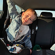 Adil is registered to the contest to win money with this photo: child, toddler, boy, car, car_seat, seatbelt, denim_jacket, smile, happy, backseat, window, sunlight, road_trip, patterned_pants, suitcase, luggage, arm, headrest, portrait, young_child