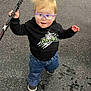 toddler, child, glasses, hoodie, jeans, shoes, hockey_stick, indoor, floor, speckled_floor, standing, person, cute, blonde_hair, casual_clothing, sports_equipment, confident, portrait, young_child, active