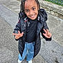 child, smiling, braided_hair, beads, black_jacket, black_top, blue_jeans, white_shoes, outdoor, pavement, peace_sign, happy, person, standing, casual_clothing, young, cute, portrait, urban, daylight