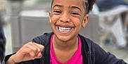 Emila participe au concours pour gagner de l'argent avec cette photo : child, girl, smiling, happy, outdoor, portrait, curly_hair, jacket, pink_shirt, chair, casual, daylight, urban, background_blur, person, seated, young, gesture, joyful, candid