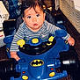 baby, child, walker, blue, batman, toy, indoor, carpet, person, cute, serious, face, clothing, striped_shirt, wheel, furniture, home, floor, head, expression