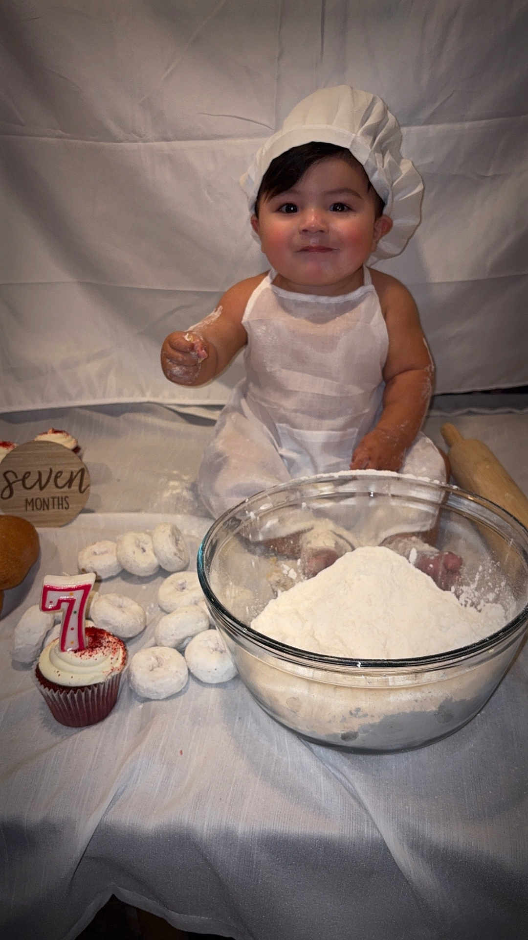 Mario joined the competition — help win amazing prizes! baby, flour, baking, cupcake, donuts, rolling_pin, white_clothing, baby_hat, tablecloth, celebration, food, powdered_sugar, smiling, portrait, sitting, kitchen, child, birthday, seven_months, cute