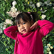 Jade is registered to the contest to win money with this photo: child, girl, portrait, pink_sweater, greenery, flowers, plants, posing, smile, young, cute, indoors, colorful, nature_background, playful, hair_tie, face, person, casual_clothing, happy