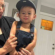 Luis Fernando Reyes joined the competition — help win amazing prizes! toddler, child, face, cap, denim_overalls, pout, adult_hand, indoor, door, window, wall, photograph_frame, person, expression, holding, nail_art, bracelet, skin, clothing, portrait
