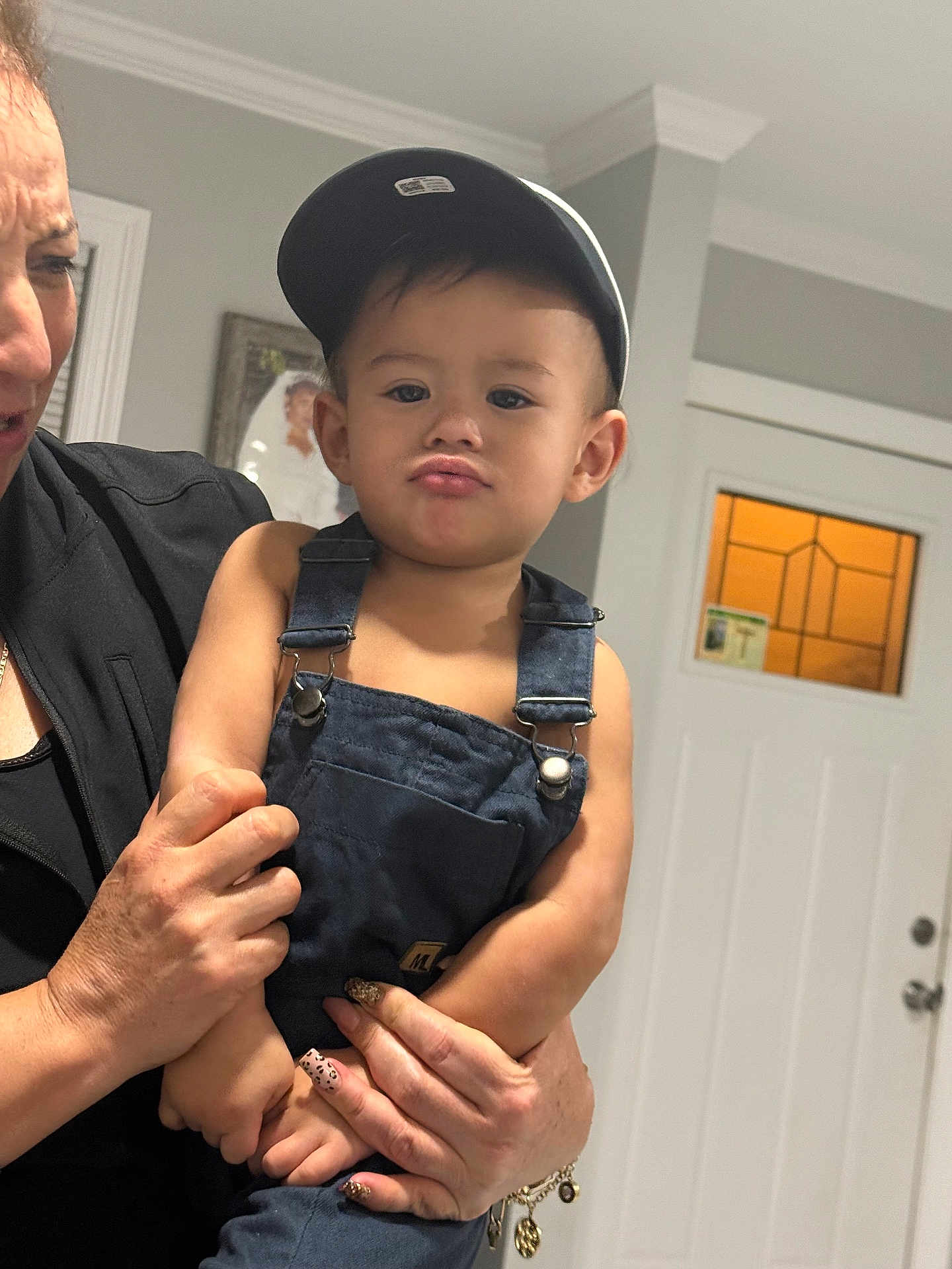 Luis Fernando Reyes joined the competition — help win amazing prizes! toddler, child, face, cap, denim_overalls, pout, adult_hand, indoor, door, window, wall, photograph_frame, person, expression, holding, nail_art, bracelet, skin, clothing, portrait
