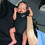 baby, newborn, sleeping, person, arm, bracelet, clothing, black_onesie, nike_logo, infant, skin, hand, foot, indoor, floor, bag, holding, resting, peaceful, casual
