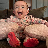 Holly is registered to the contest to win money with this photo: baby, child, smile, happy, couch, pillow, footwear, onesie, indoor, face, infant, red_socks, home, furniture, cozy, portrait, sitting, cute, expression, person