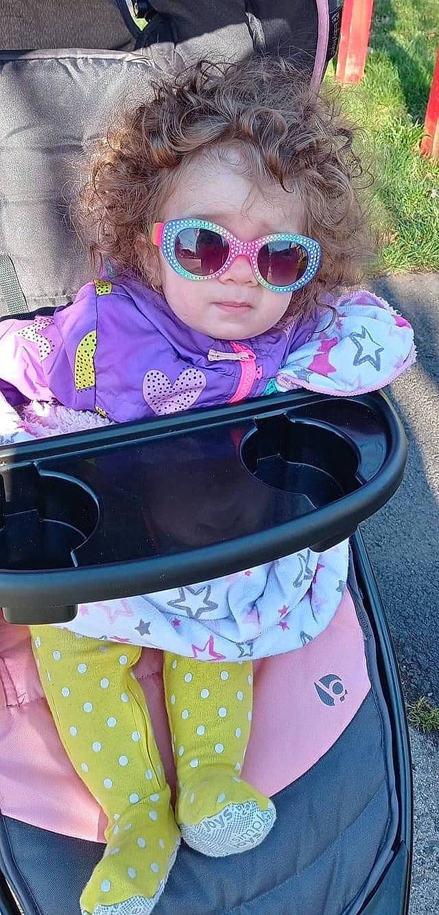 Leia is registered to the contest to win money with this photo: baby, baby_carriage, baby_toddler_clothing, eye, eyewear, glasses, goggles, green, magenta, person, personal_protective_equipment, photograph, pink, plant, purple, sleeve, sunglasses, toddler, violet, vision_care
