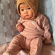Eloise joined the competition — help win amazing prizes! baby, child, infant, pink_outfit, bear_hat, hat_with_ears, cute, indoors, couch, blanket, textured_blanket, seated, portrait, looking_away, soft_lighting, warm_colors, clothing, fuzzy_hat, expression, young_child