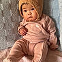 baby, child, infant, pink_outfit, bear_hat, hat_with_ears, cute, indoors, couch, blanket, textured_blanket, seated, portrait, looking_away, soft_lighting, warm_colors, clothing, fuzzy_hat, expression, young_child
