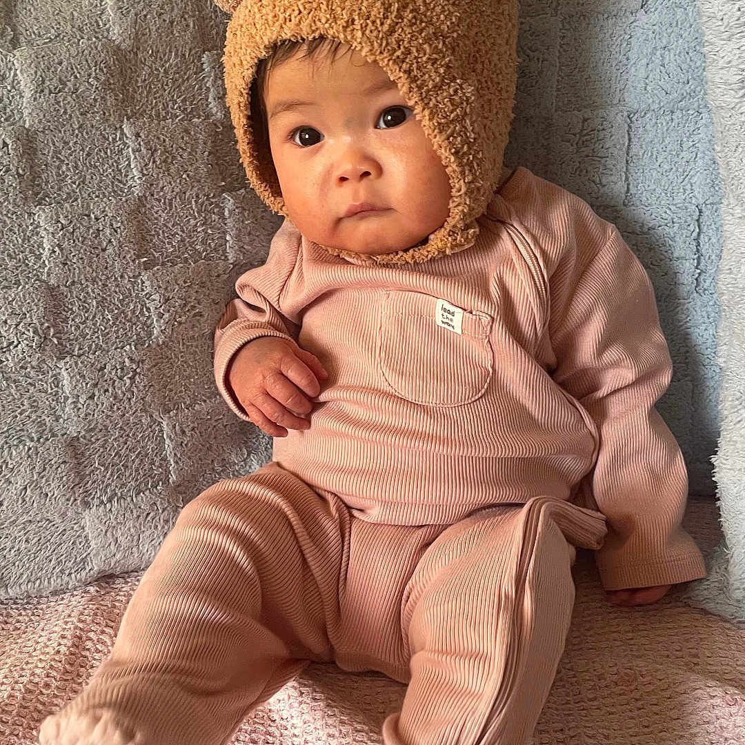 Eloise joined the competition — help win amazing prizes! baby, bear_hat, blanket, child, clothing, couch, cute, expression, fuzzy_hat, hat_with_ears, indoors, infant, looking_away, pink_outfit, portrait, seated, soft_lighting, textured_blanket, warm_colors, young_child