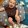 Jameson joined the competition — help win amazing prizes! baby, smiling, infant, pillow, toy, carpet, floor, clothing, black_shirt, red_letters, sitting, happy, cute, indoor, child, playtime, cushion, colorful, person, home