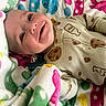 baby, infant, smile, blanket, colorful, polka_dot, clothing, onesie, milk_bottle, pacifier, face, happy, cute, child, portrait, lying_down, soft_texture, warm, cozy, expression