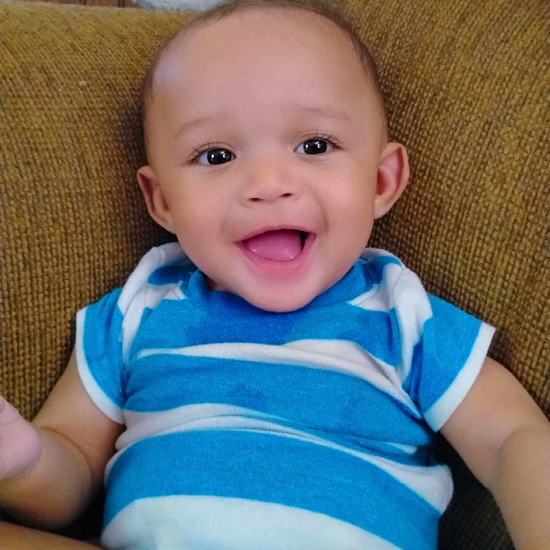 Grant-Ezra is registered to the contest to win money with this photo: baby, blue_striped_onesie, casual_clothing, child, comfortable, couch, cute, face, happy, home, indoor, infant, joyful, one_person, person, portrait, sitting, skin, smiling, young_child