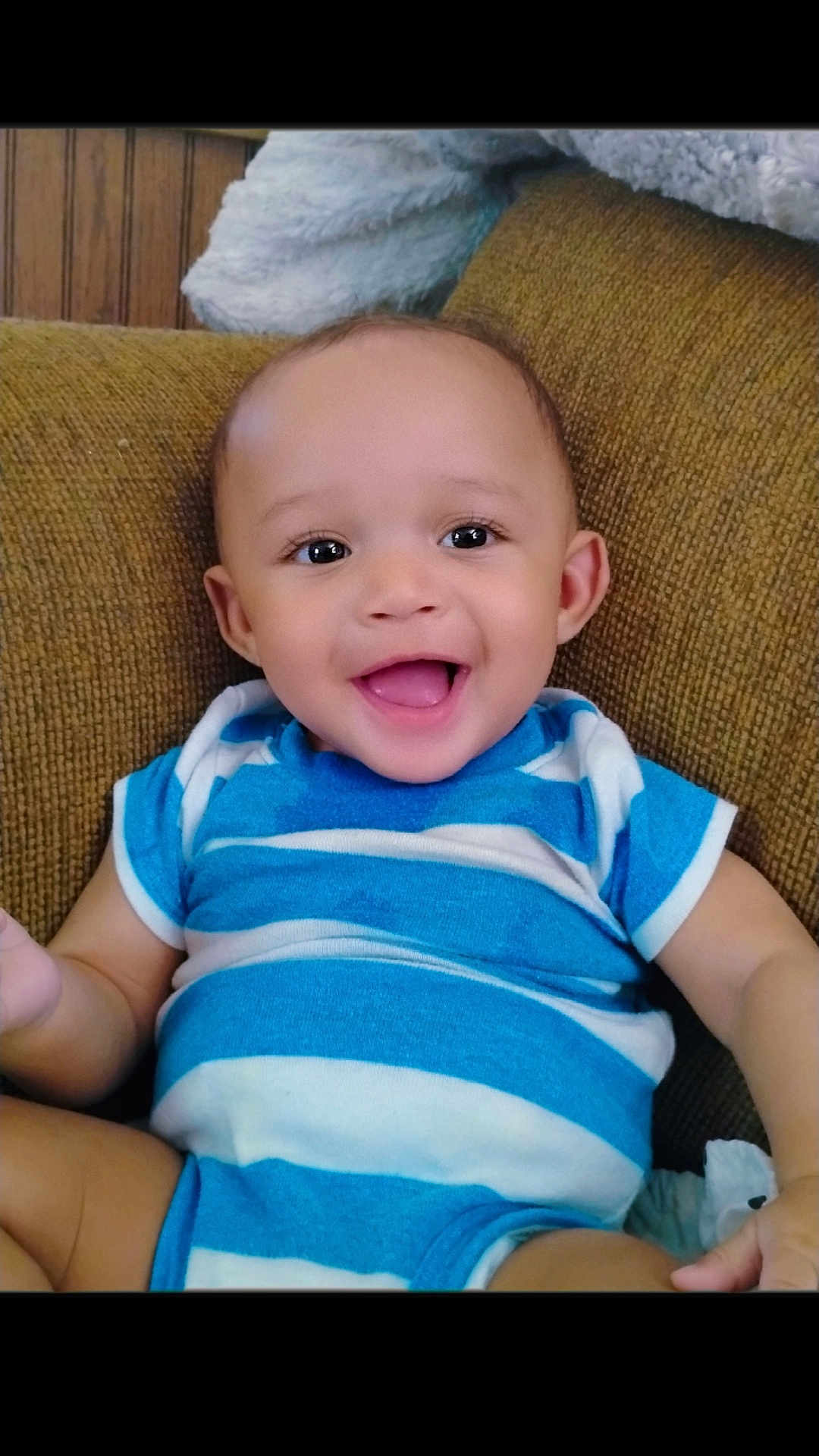 Grant-Ezra is registered to the contest to win money with this photo: baby, smiling, happy, infant, blue_striped_onesie, couch, indoor, child, portrait, cute, young_child, sitting, face, skin, person, one_person, casual_clothing, home, comfortable, joyful