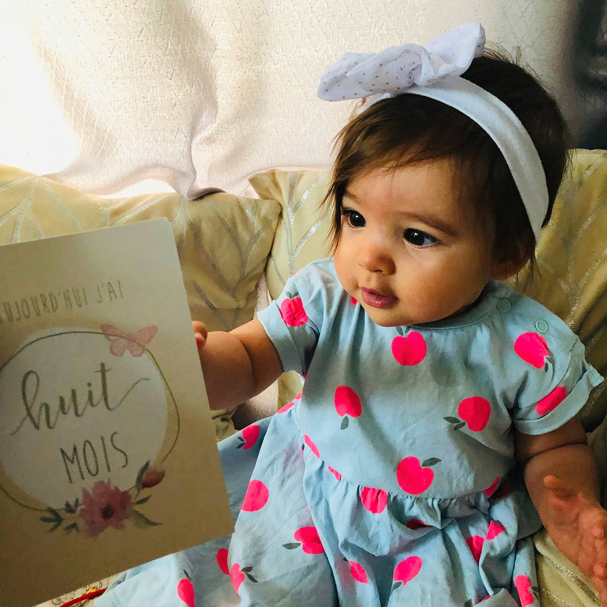 Emma participe au concours pour gagner de l'argent avec cette photo : baby, baby_toddler_clothing, book, cap, child, dress, eye, face, handwriting, happy, head, human, mammal, person, product, skin, sleeve, smile, textile, toddler