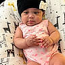 baby, infant, child, portrait, sitting, lying_down, beanie, bow, pink_outfit, onesie, giraffe_pattern, cushion, indoor, close_up, face, hands, arms, legs, looking_at_camera, safe