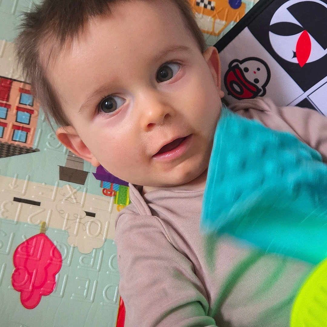 Adrián a rejoint le concours — aidez-le/la à gagner de superbes lots ! bright_eyes, candid, casual_clothing, child, closeup, colorful, curious, face, happy, indoor, infant, patterned_background, person, playmat, portrait, small_hands, soft_lighting, toddler, toy, young_child