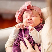Kinsley is registered to the contest to win money with this photo: baby, infant, sleeping, headband, bow, purple_dress, hands, person, arm, cozy, smiling, cute, portrait, indoor, soft_light, closeup, newborn, child, holding, warm