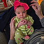 Kinsley is registered to the contest to win money with this photo: baby, infant, child, pink_bow, green_onesie, ladybug_pattern, hands_clasped, adult_hands, gray_shirt, star_pattern, living_room, table, red_cup, baby_swing, seated, curious_expression, polka_dots, cozy, indoor, portrait